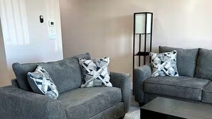 Ein Wohnzimmer mit zwei grauen Sofas, gemusterten Kissen, einem schwarzen Couchtisch und einem Teppich mit Muster.