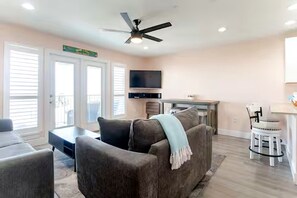 A living room with a sofa, a coffee table, a TV, and a ceiling fan. - Adorable 1-bedroom condo steps from the beach in Perdido Key - Sleeps 6!! (Pensacola)