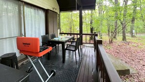 Un espacio al aire libre cubierto con una parrilla, mesa de comedor, sillas y vistas a un bosque.