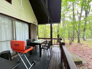 A covered outdoor area with a grill, dining table, chairs, and a view of a forest. - Karuizawa Forest Base1 KF1 (Kamahara, Tsumagoi-mura, Agatsuma-gun)