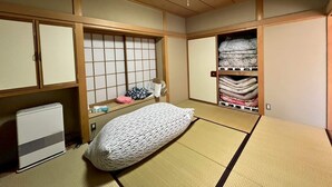 Una habitación tradicional japonesa con suelo de tatami, futón, calentador y un mueble de almacenamiento con textiles doblados.