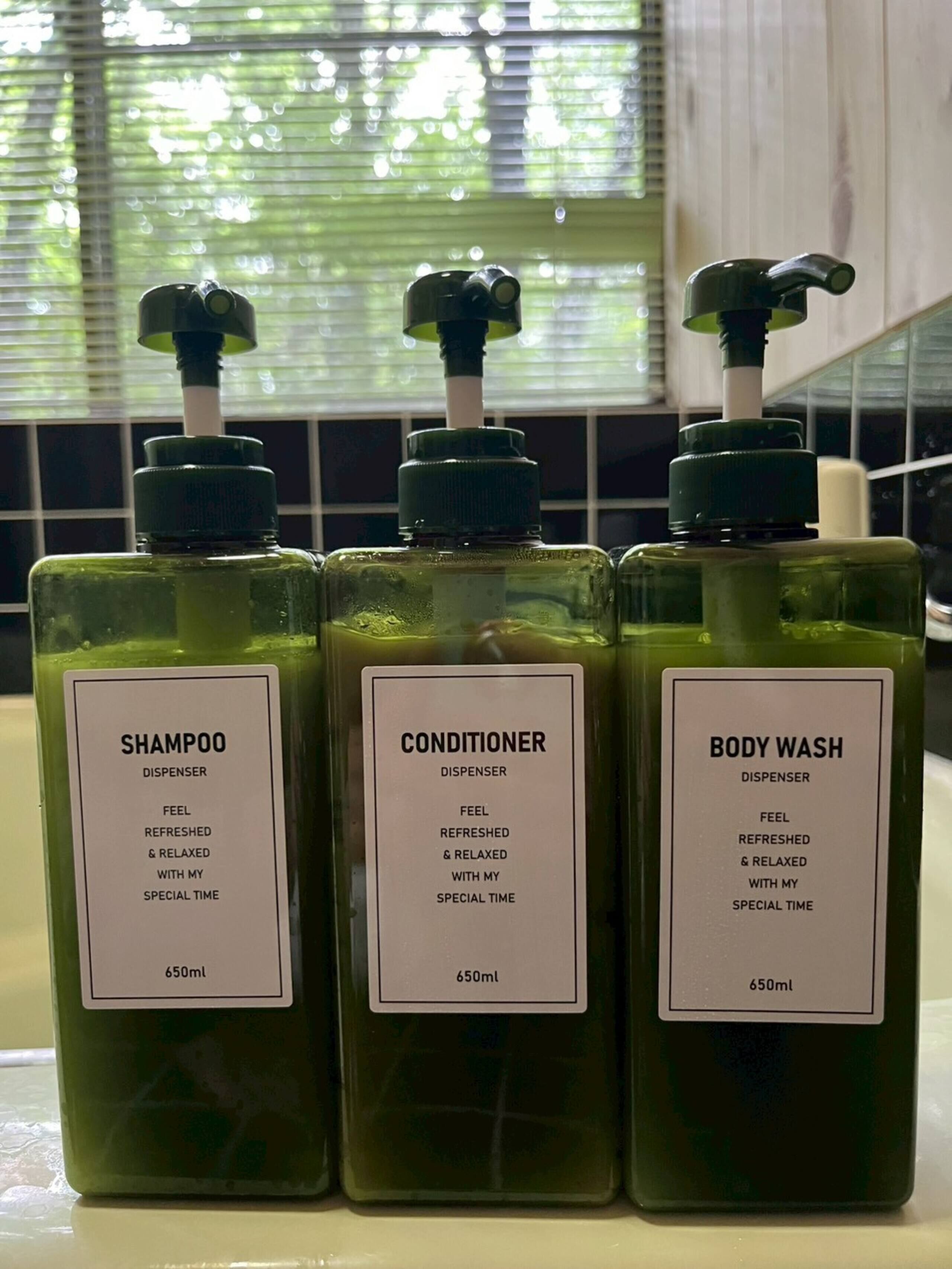 Tres dispensadores de 650 ml de champú, acondicionador y gel de baño sobre una encimera.