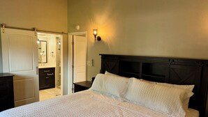 Camera da letto con un letto, un comodino, una lampada a muro e una porta che conduce al bagno.