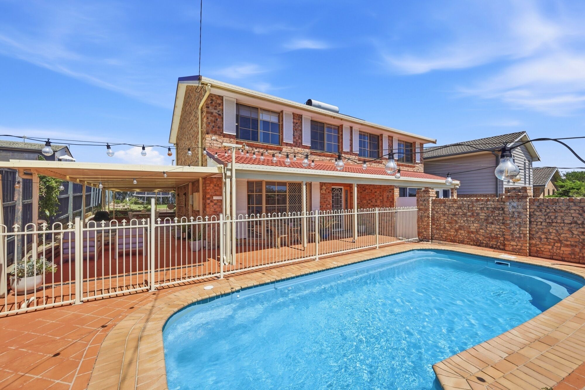 Une maison à deux étages avec une piscine, un patio couvert et une clôture blanche.