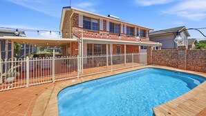 A two-story house with a swimming pool, a covered patio, and a white fence.