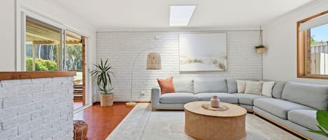Een moderne woonkamer met een grijze modulaire bank, een ronde salontafel van riet en een witte bakstenen muur.