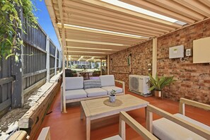 Un patio al aire libre con pared de ladrillo, mesa de madera, sofá y una parrilla.