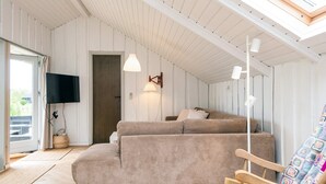 Et hyggeligt værelse med en sofa, en træstol, et fjernsyn og en loftlampe.