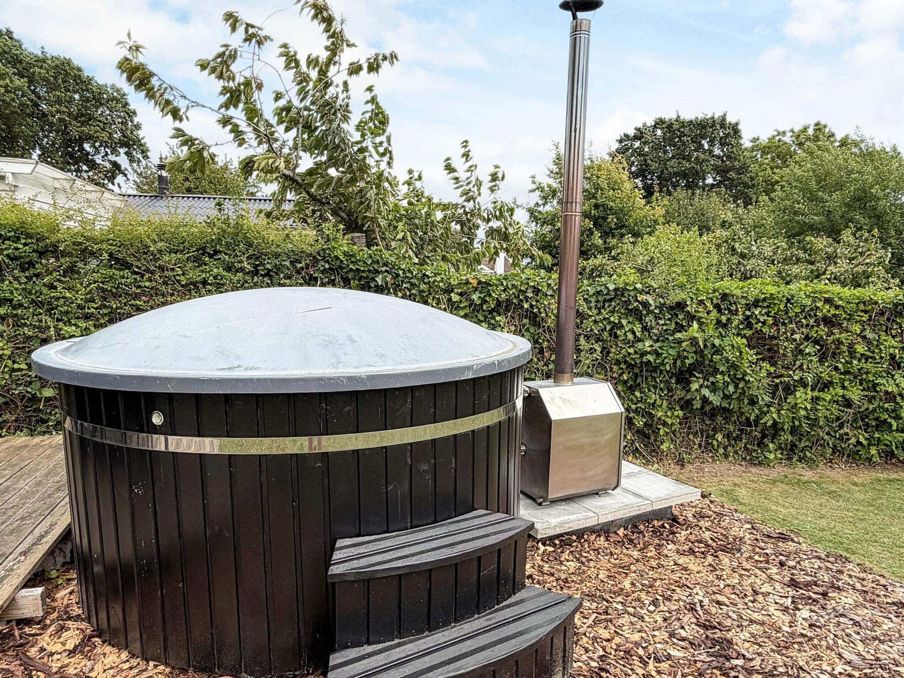 A cylindrical outdoor heater with a flat top, a metal pole, and a small box on a platform with steps leading up to it.
