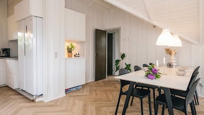 Et moderne køkken med hvide skabe, et indbygget køleskab og et spiseområde med et hvidt bord og sorte stole.