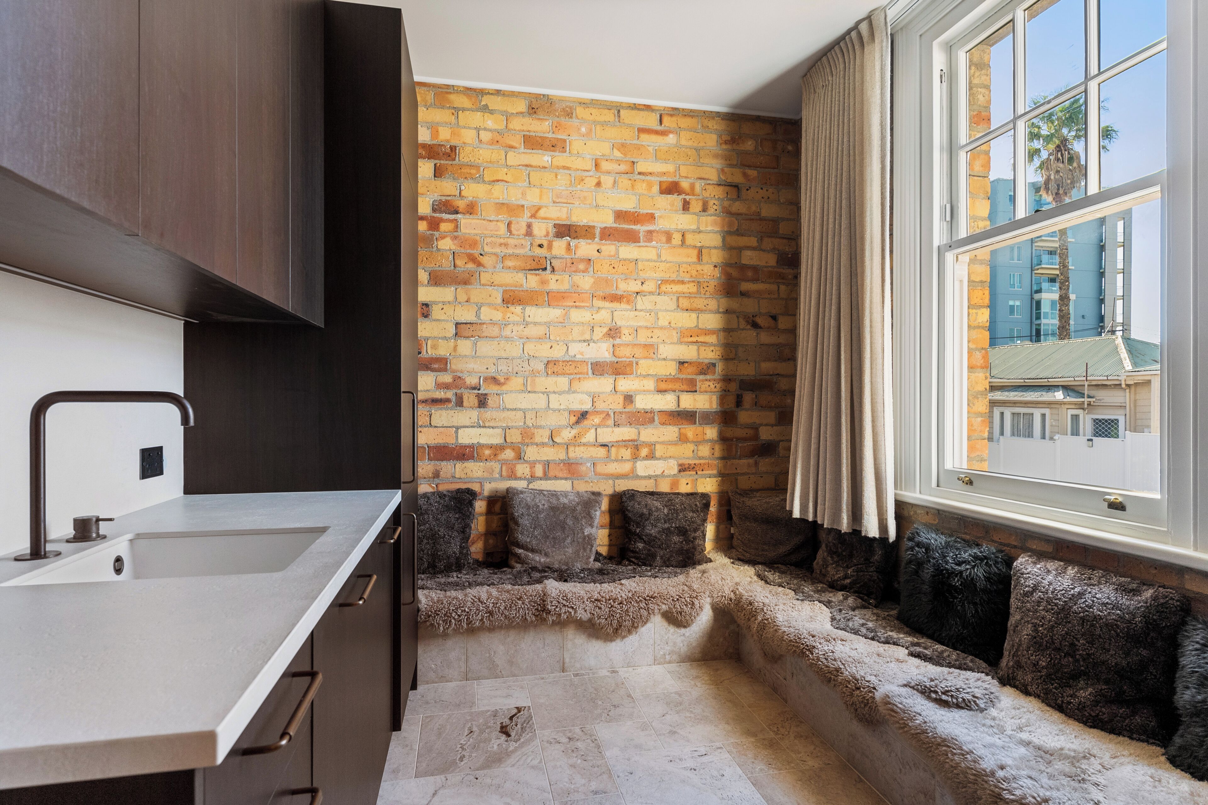 A kitchen with a brick wall, a window with curtains, and a built-in bench with cushions.