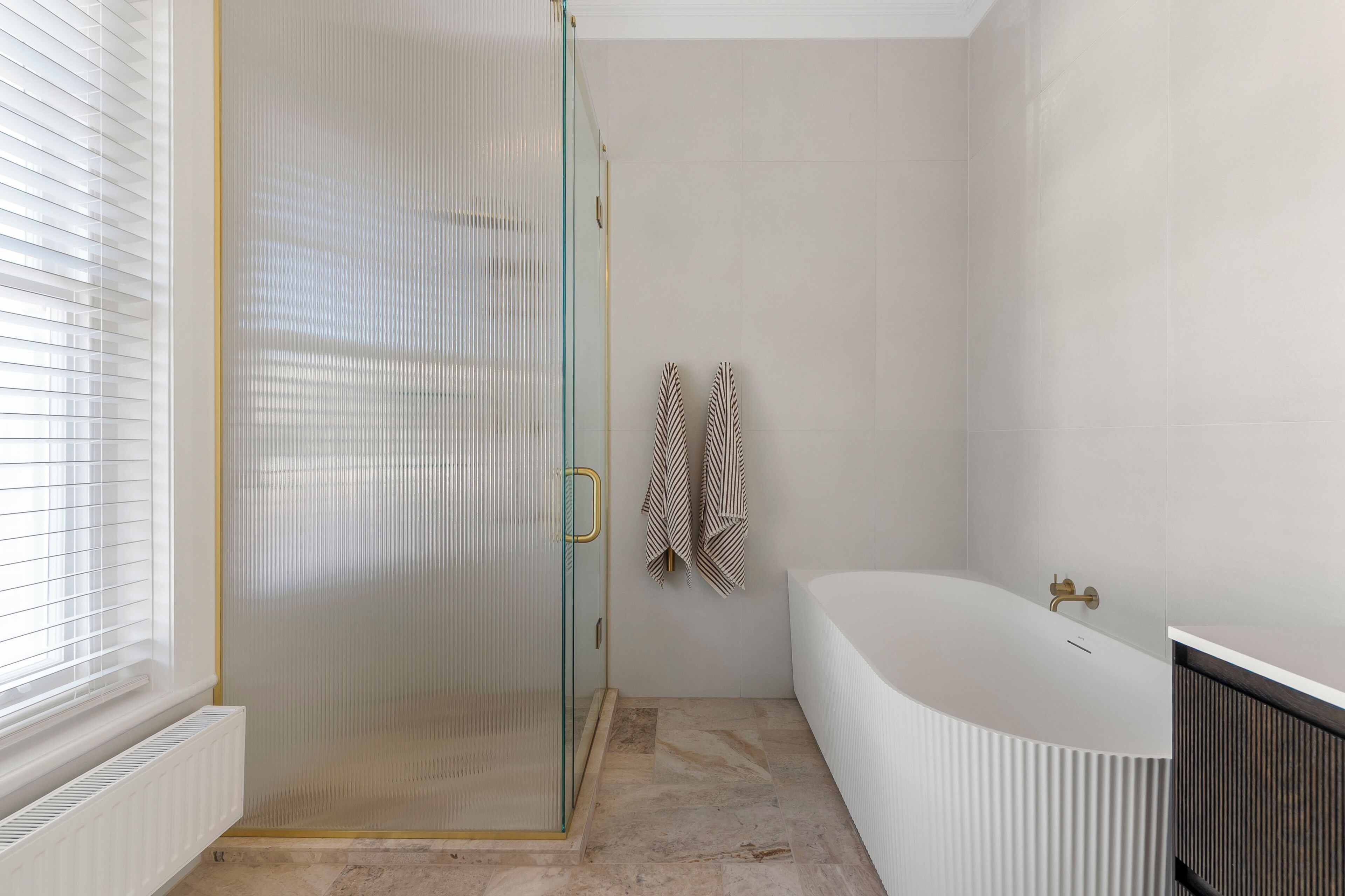 Ein modernes Badezimmer mit einer gläsernen Duschkabine, einer freistehenden Badewanne und einem Handtuchhalter mit gemusterten Handtüchern.
