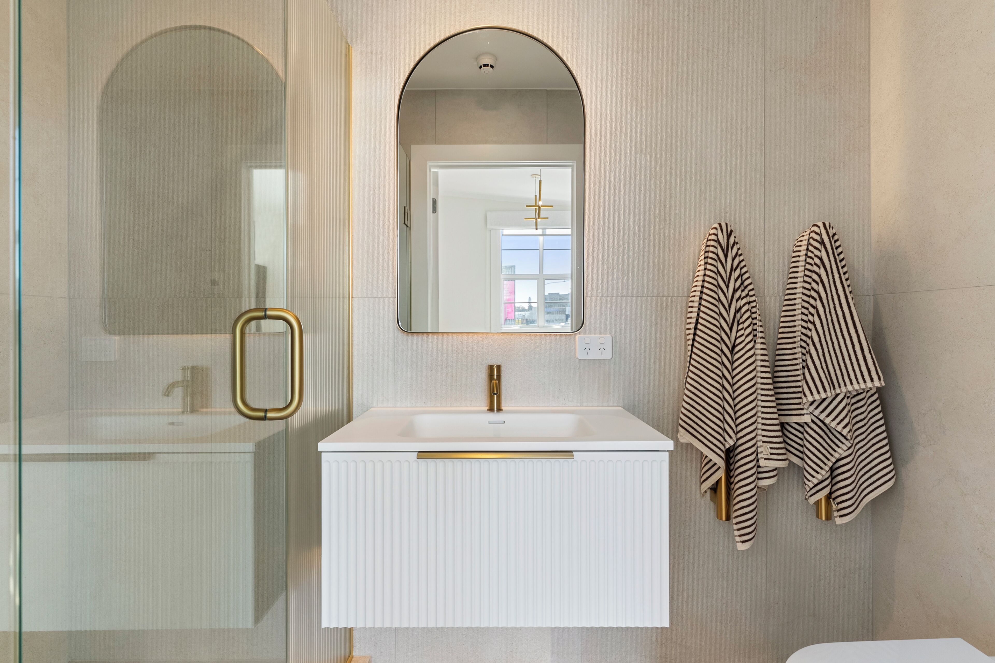 A bathroom with a white sink, a gold faucet, a mirror with an arched top, and striped towels hanging on the wall.