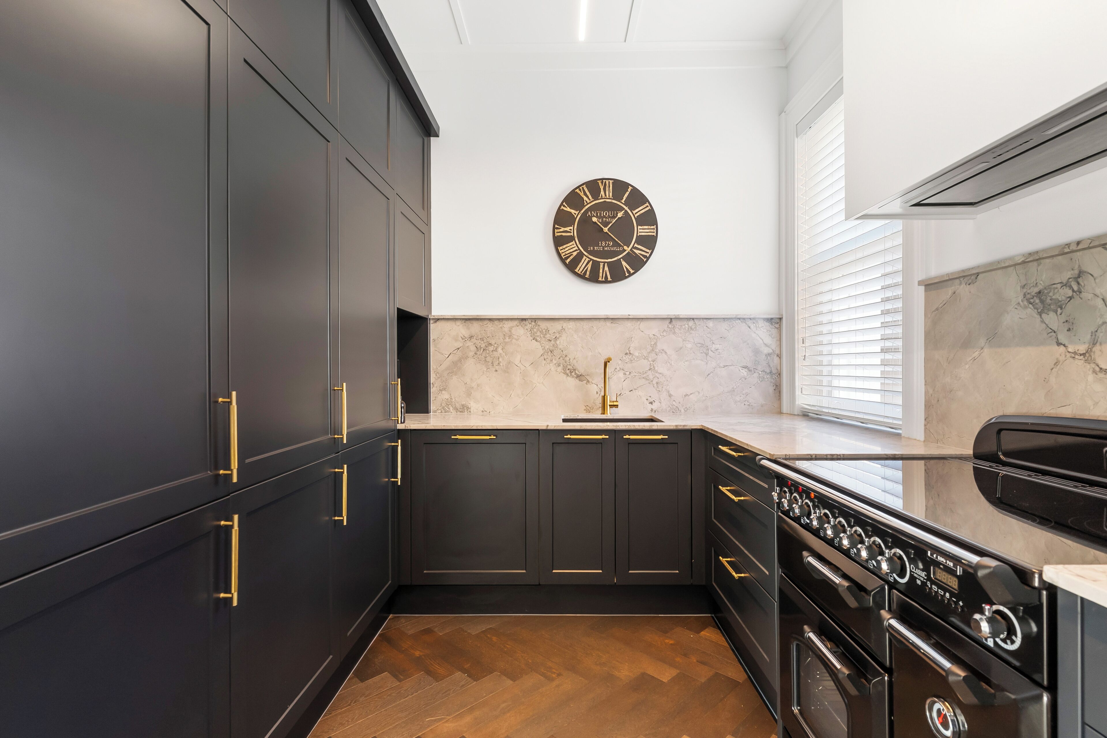 Eine moderne Küche mit dunklen Schränken, einer Marmor-Spritzschutzwand, einer Wanduhr und einem eingebauten Backofen.