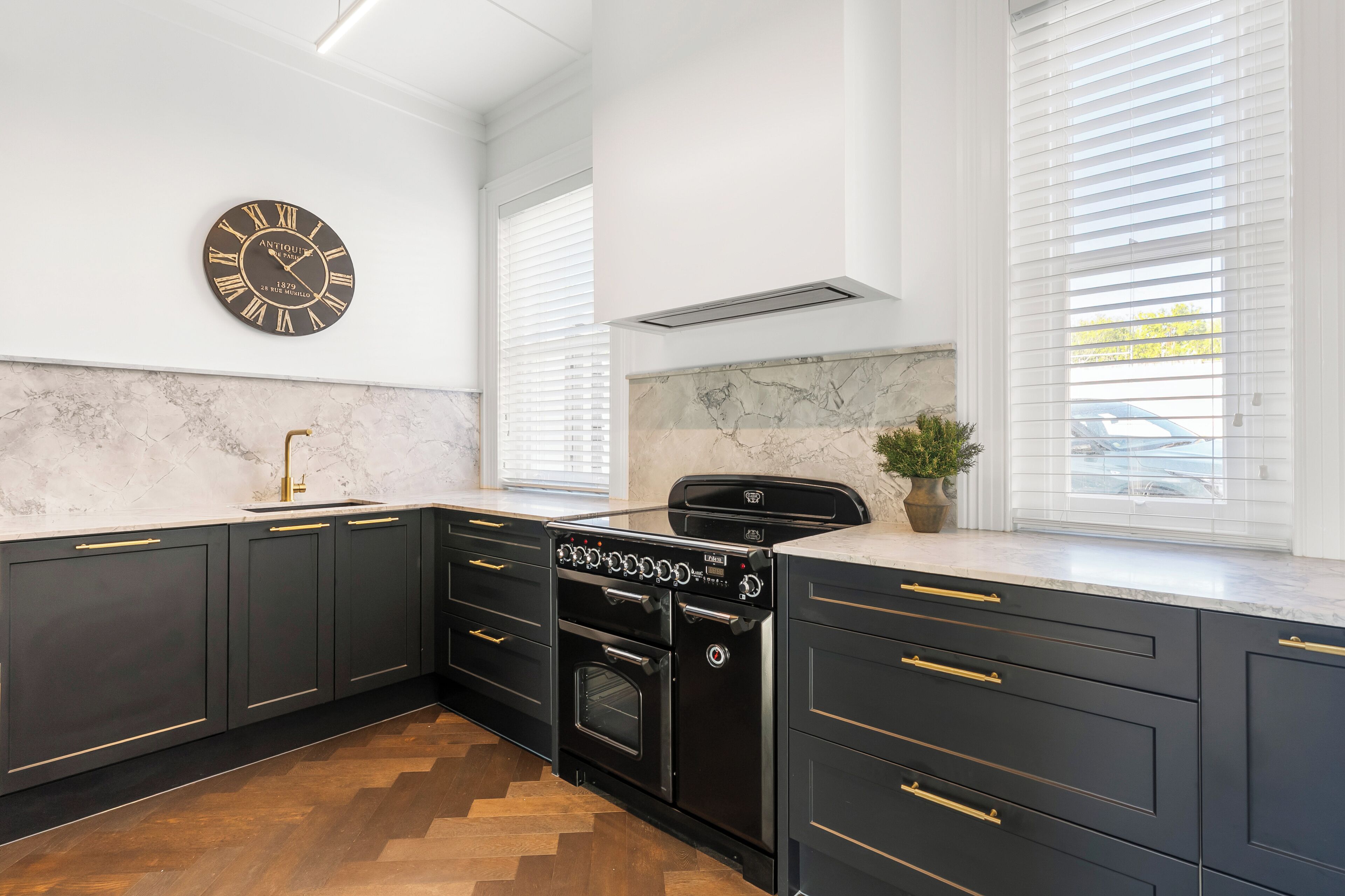 A kitchen with dark cabinetry, a black stove, a marble backsplash, and a wall clock.