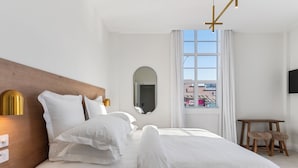 Habitación de hotel con una cama grande, cabecera de madera, mesita de noche con lámpara, una pequeña mesa con una silla y un televisor montado en la pared.
