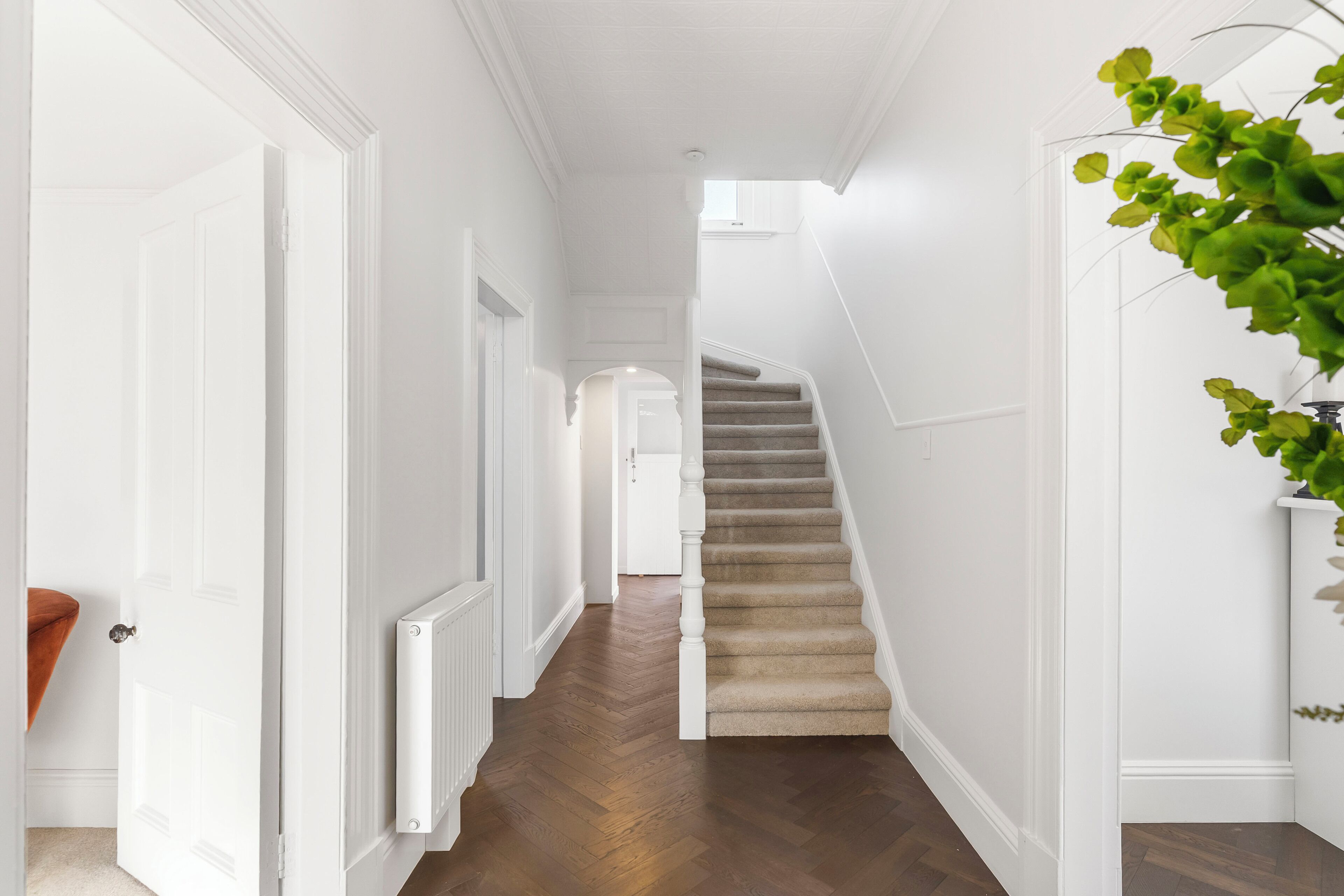 A hallway with a wooden floor, white walls, a staircase, and a door.
