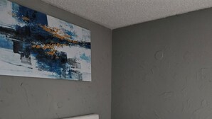 A bedroom with a bed, a painting on the wall, and a textured wall.