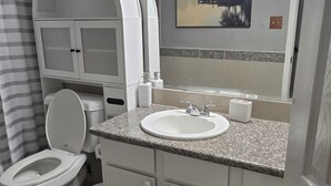 A bathroom with a toilet, sink, vanity, and a shower area.