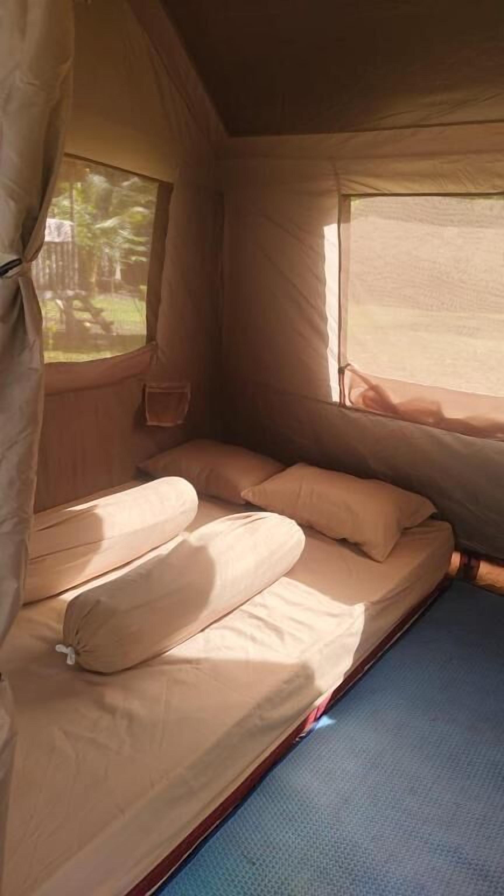 A tent interior with a bed, a small window, and a blue mat.