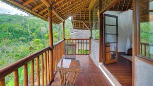 Un balcón de madera con una mesa de vidrio, con vistas a un paisaje verde y exuberante.