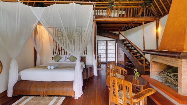 Una habitación con cama, una silla de madera, una mesa y una chimenea.