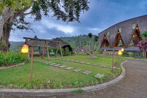 Um edifício de estilo tradicional com telhado de colmo, rodeado por um jardim bem cuidado com caminhos de pedra.