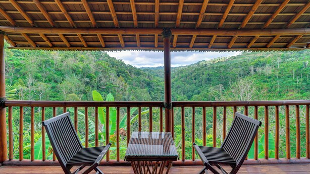 Una terraza de madera con dos sillas y una mesa, con vistas a un valle verde exuberante.