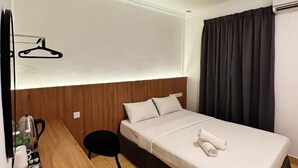 Quarto de hotel com cama, escrivaninha com cadeira, cabideiro e janela com cortinas.