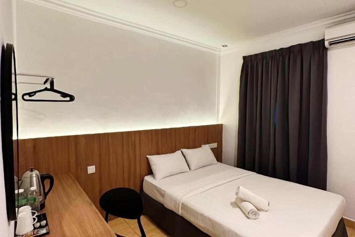 Une chambre d’hôtel comprenant un lit, un bureau avec une chaise, un porte-manteau et une fenêtre avec des rideaux.