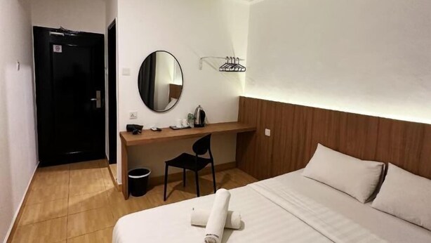 Quarto de hotel com cama, escrivaninha, cadeira, espelho e porta preta.