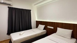 Quarto de hotel com duas camas, uma cortina escura, um painel de cama branco e um ar condicionado fixado na parede.