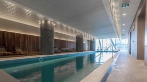 En moderne indendørs swimmingpool med et træbeklædt område til reception og store søjler.