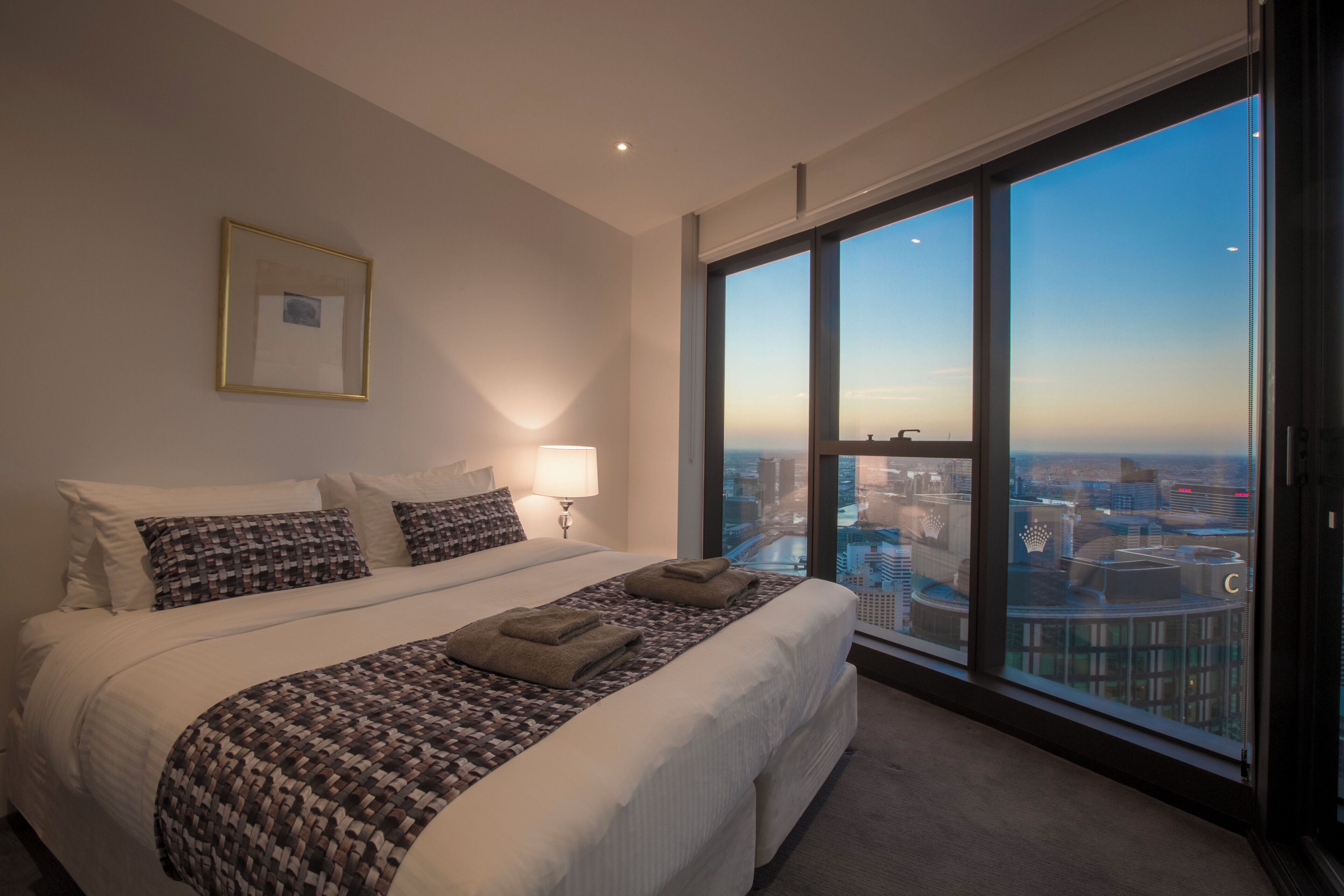 Quarto de hotel com uma cama grande, vista para a cidade e um quadro na parede.