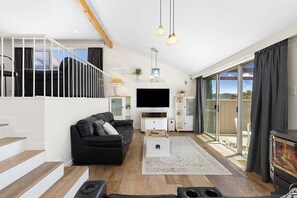 Una sala de estar moderna con un sofá negro, un televisor de pantalla plana, una chimenea y una escalera que conduce a un nivel superior.