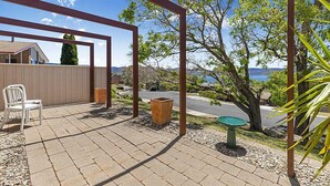 Une terrasse agrémentée d’une pergola, d’une chaise blanche, d’un jardinière et d’un abreuvoir à oiseaux.