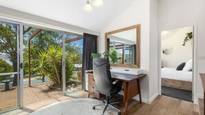 Ein modernes Schlafzimmer mit einem großen Bett, einem Schreibtisch und Blick auf einen Garten durch Glastüren.