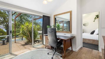 A modern bedroom with a large bed, a desk, and a view of a garden through glass doors.