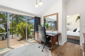Un dormitorio moderno con una cama grande, un escritorio y vistas a un jardín a través de puertas de cristal.