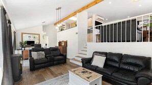 Ein modernes Wohnzimmer mit Kamin, zwei schwarzen Ledersofas, einem Couchtisch und einer Treppe, die zu einer oberen Ebene führt.