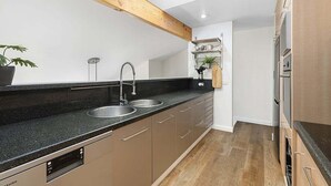 Une cuisine moderne avec un plafond orné de poutres en bois, des éviers en acier inoxydable et un lave-vaisselle encastré.