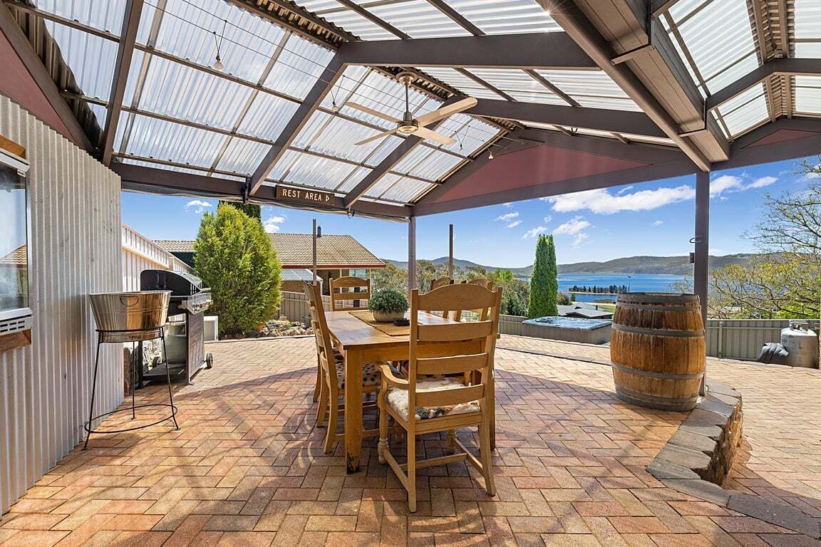 A covered patio with a table and chairs, a barbecue grill, and a view of the landscape.