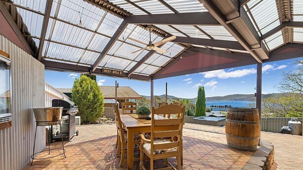 Eine überdachte Terrasse mit Tisch, Stühlen, einem Grill und Blick auf die Landschaft.
