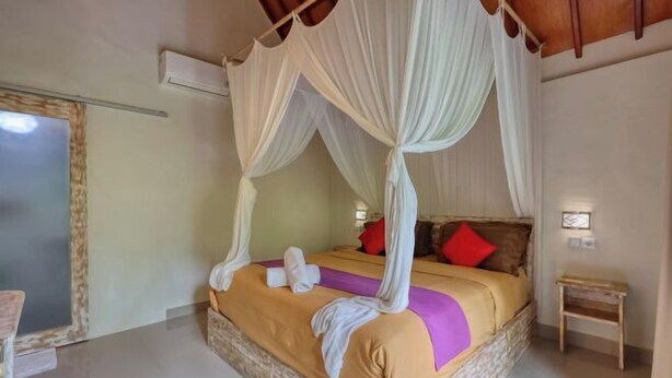 A four-poster canopy bed with a woven base, a small bedside table, and a wall-mounted light fixture.