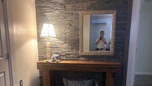 Et værelse med en stenvæg, en træbænk, et spejl, en lampe og et mønstret tæppe.