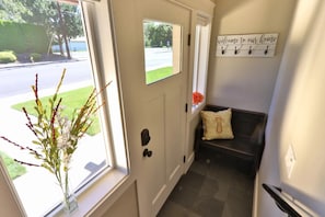 A hallway with a door, a bench, a wall-mounted sign, and a window with a plant.