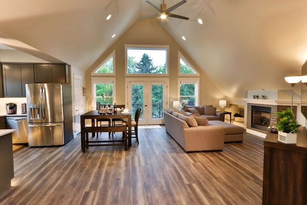 A spacious loft with a dining area, kitchen, and living space, featuring a large window and a fireplace.
