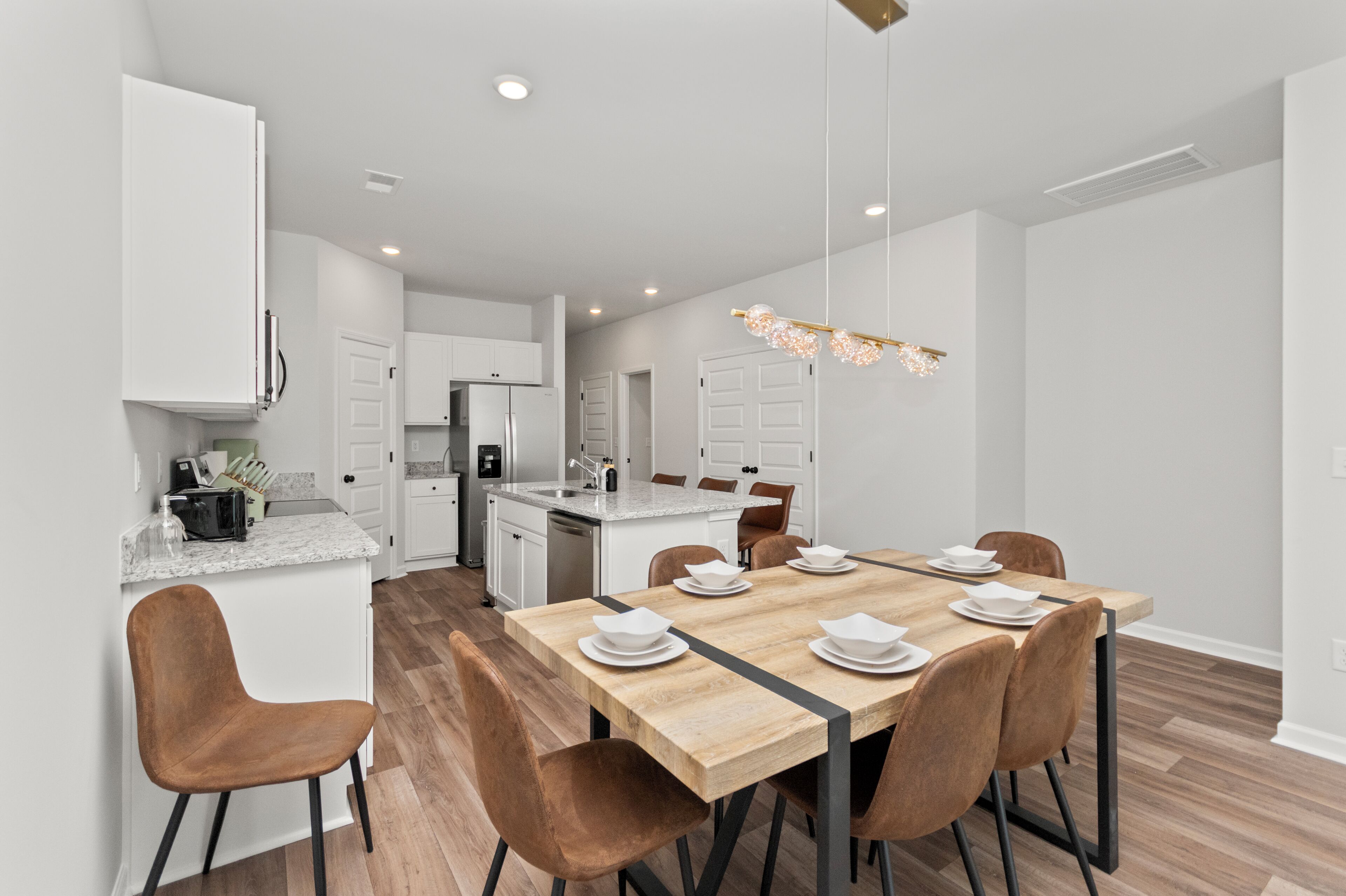 A modern kitchen with white cabinetry, a wooden dining table set for four, and a central island with a sink.