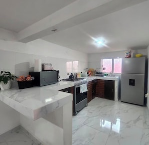 A modern kitchen with a marble countertop, a gas stove, a refrigerator, and a sink.