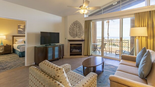 Una habitación de hotel con sofá, televisión, chimenea y balcón con vistas.